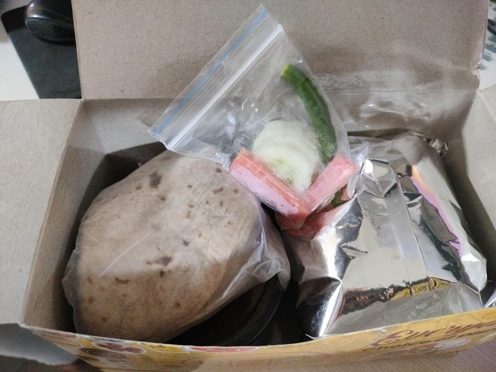 A tiffin box opened to show fresh roti, vegetables and pickle